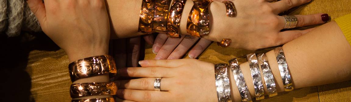 Hands wearing carved copper and silver bracelets