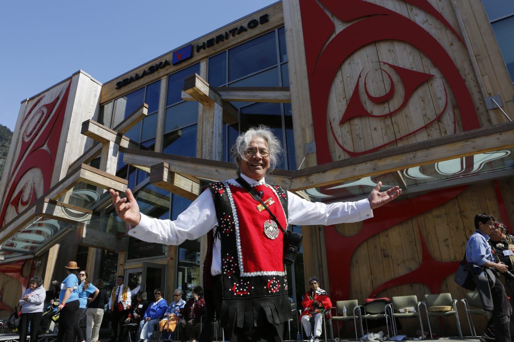 An Elder stands with open arms outside the Walter Soboleff Building.