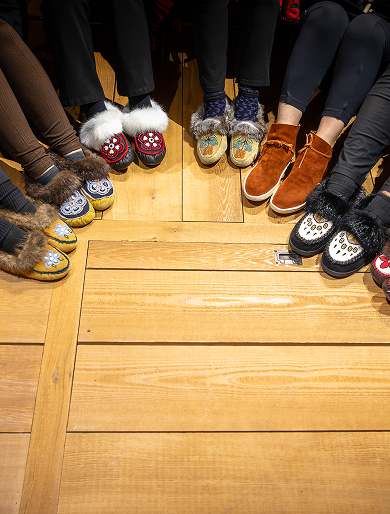 People form a circle while wearing decorated moccasins.