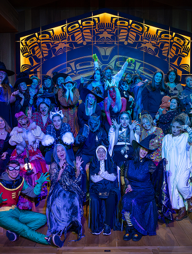 A large staff group gathers in front of an illuminated clan house screen.