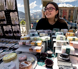 A Native artist sells jewelry, soap, and other handmade goods at an outdoor market table
