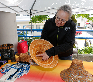 A Native artist displays a woven cedar hat at an outdoor market table