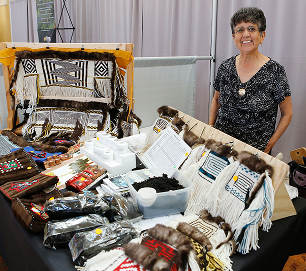 A Native artist stands behind a table of woven and beaded artwork