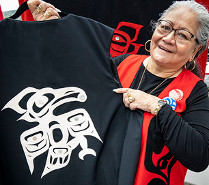 A Native artist displays a black garment with a white Northwest Coast design