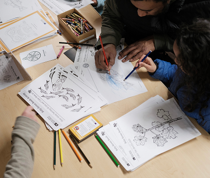 Children draw and color classroom activity sheets with an educator