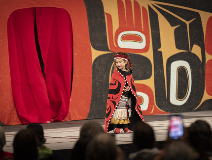 A young child models red and black regalia on the Celebration stage