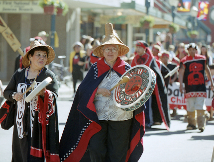 Two women wearing woven hats and traditional regalia walk in the Celebration parade