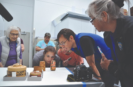 Artists examining small carved and woven artworks around a worktable
