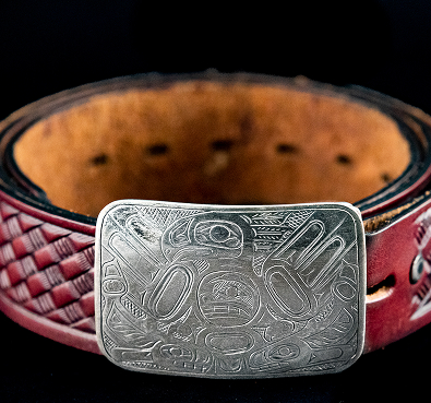 A carved silver buckle on a woven red belt