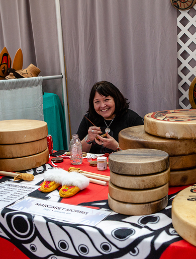 An artist painting a hand drum at an art market table