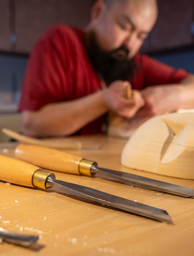 An artist carving wood with chisels in the foreground