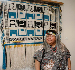 An artist stands beside a large woven black, white, and blue textile