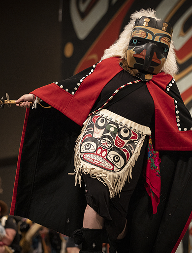 A dancer wearing a carved mask and red regalia at Celebration