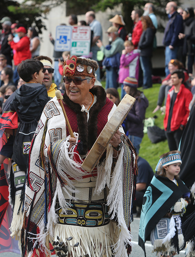 A Celebration participant wearing regalia and carrying a hand drum