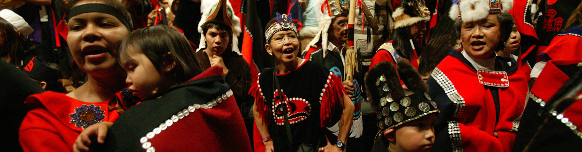 Adults and children singing and dancing together in red and black regalia