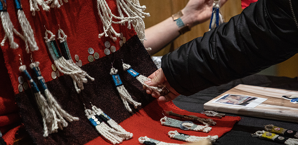Visitor examining handmade regalia and artwork at an artist table