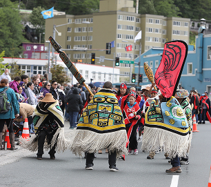 Parade participants display woven hats, button blankets, and carved staffs