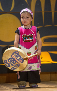 A young child models pink regalia and holds a hand drum at Celebration