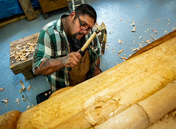 A master carver shaping a cedar log with an adze