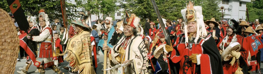 Celebration participants in traditional regalia march together through downtown Juneau