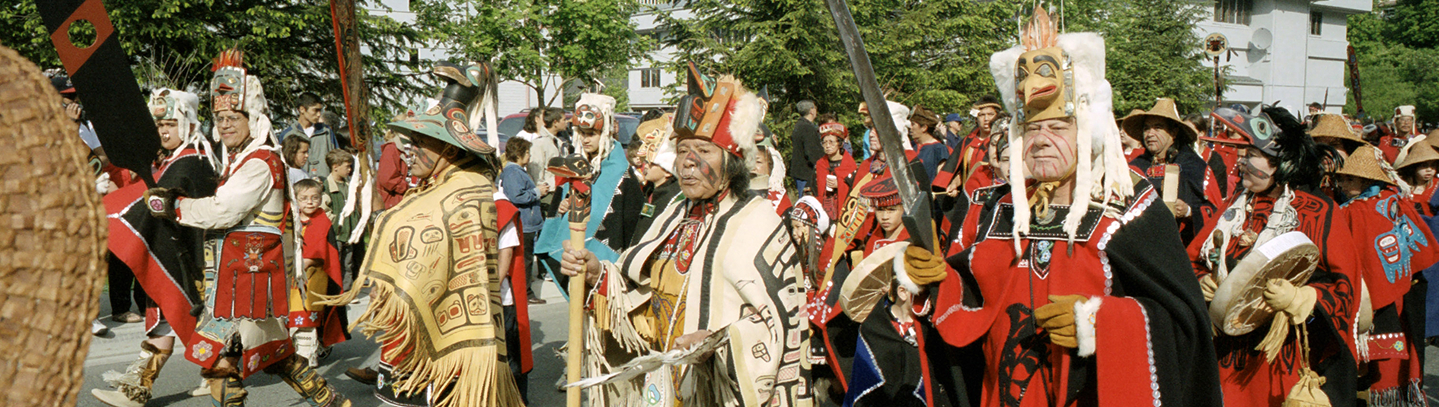 Celebration participants in traditional regalia march together through downtown Juneau