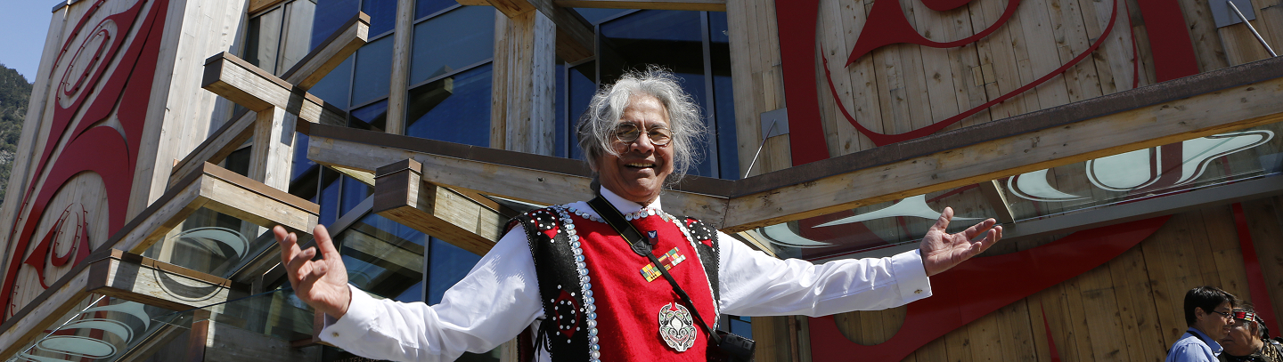 A smiling Elder in regalia welcoming visitors outside the Walter Soboleff Building