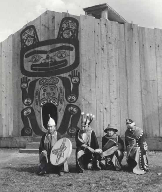 Four clan leaders in regalia gathered before a painted clan house front