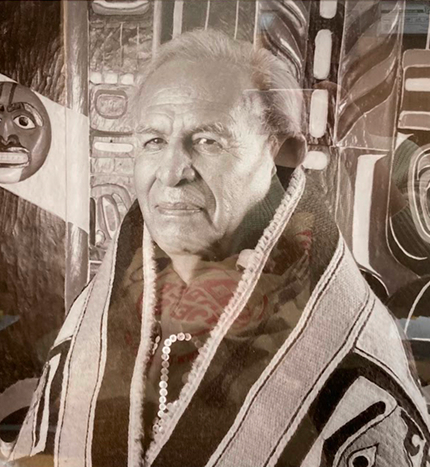 Tlingit leader Judson L. Brown wearing regalia in front of Northwest Coast artwork