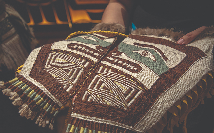 Hands examining a woven Northwest Coast textile with a geometric animal design