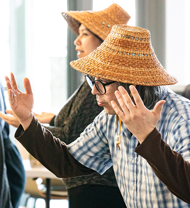 Performers wearing woven hats rehearsing hand gestures