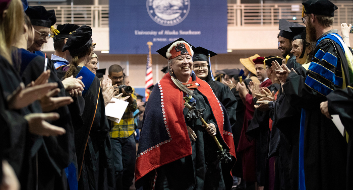 Graduate in Northwest Coast regalia walking between applauding faculty