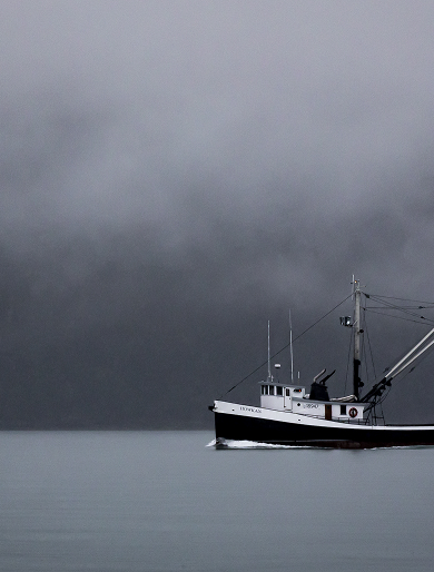 A fishing vessel crossing calm water beneath a misty sky