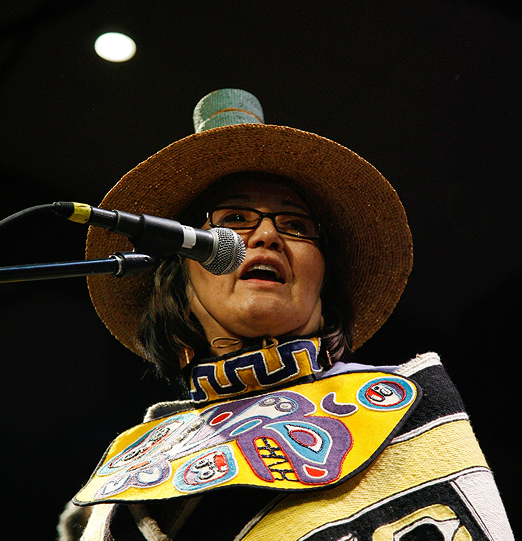 Rosita Kaaháni Worl speaking at a microphone in regalia and a woven hat.