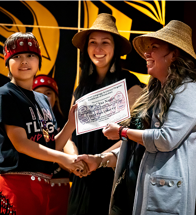 A student receives a certificate from two educators wearing woven hats