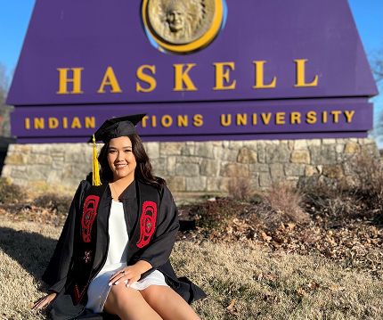 A Sealaska scholarship graduate seated in front of the Haskell Indian Nations University sign