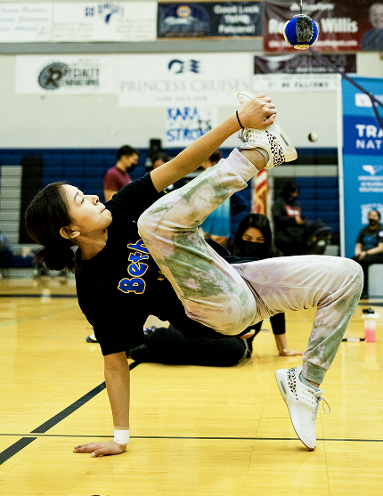 An athlete balancing on one hand while kicking a suspended ball