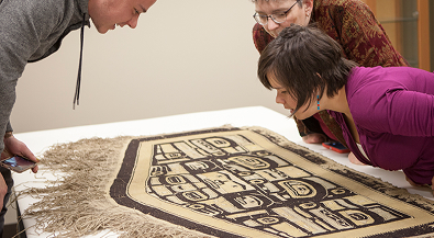 Researchers examining a woven Chilkat robe