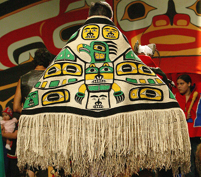 A dancer wearing a fringed robe decorated with colorful Tlingit clan crests