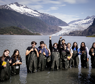 Students standing in shallow water with a glacier and mountains behind them