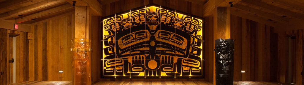 Illuminated amber-and-black glass house screen and warrior posts inside Shuká Hít