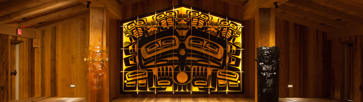 Illuminated amber-and-black glass house screen and warrior posts inside Shuká Hít