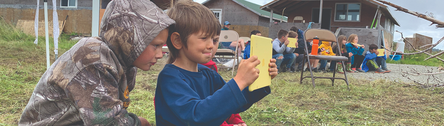 Two children using a tablet during an outdoor cultural camp