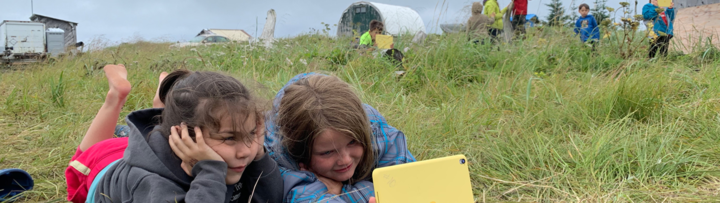 Two students using a tablet while learning outdoors in a grassy field