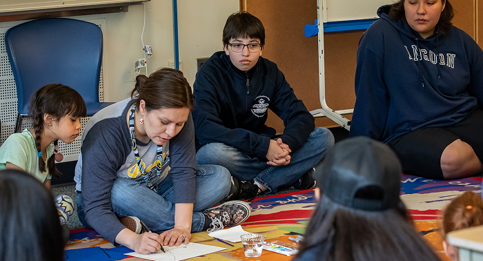 An educator writes on paper with students seated in a classroom circle