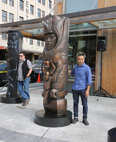 Tlingit artist Jackson Polys beside his bronze Mother of Raven house post