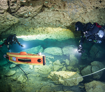 Divers guide an underwater survey vehicle through a submerged cave