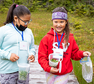 Two students carrying gathered plants during an outdoor activity