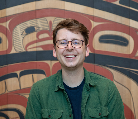 A visiting scholar smiling in front of a Northwest Coast artwork