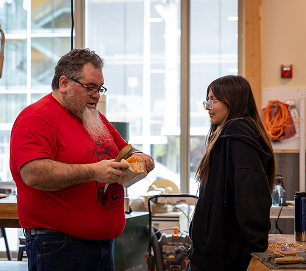 An instructor showing a carved wooden bowl to an Atnané Academy student