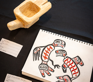 A carved wooden bowl displayed beside a student formline design